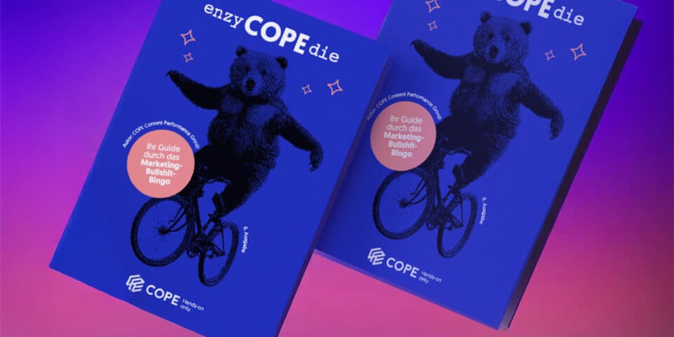Zwei blaue Bücher mit dem Titel "enzyCOPEdie", auf deren Cover ein Bär auf einem Fahrrad fährt, vor einem Hintergrund mit lila und rosa Farbverlauf.